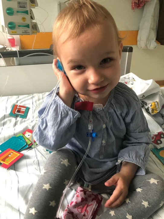 Die zweijährige Victoria sitzt auf einem Krankenhausbett.