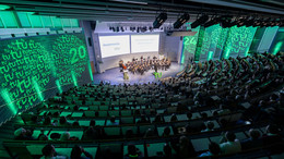 Dezember Das Bild zeigt das Audimax der TU Dortmund bei der Akademischen Jahresfeier 2024. Das Foto wurde von oben aufgenommen und zeigt das Publikum von hinten. Im Zentrum, weiter oben im Bild ist das Orchester der TU Dortmund zu sehen, darüber die Präsentation. Die seitlichen Wände des Audimax sind grün angestrahlt und werden zusätzlich auf beiden Seiten mit zwei Kreisen, in denen das TU-Logo sowie die Zahl 24 angezeigt wird, angestrahlt.