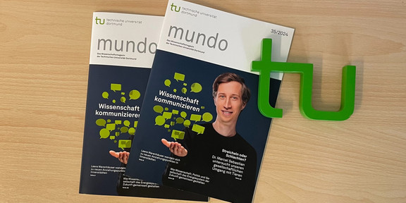 Zwei Exemplare der neuen mundo-Ausgabe liegen auf einem Tisch, daneben ein TU-Logo
