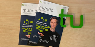 Zwei Exemplare der neuen mundo-Ausgabe liegen auf einem Tisch, daneben ein TU-Logo