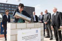 Several people stand around a brick cube. A woman is sinking a time capsule.