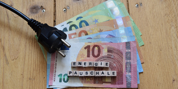 auf Holzdielen liegen Geld und ein Kabel mit Stecker, darauf der Schriftzug "Energiepauschale"