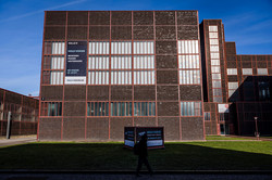 Foto: Ein großes Backsteingebäude mit Fenstern und Bannern, die auf die Ausstellung „HOLO-VOICES“ hinweisen.