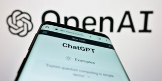 ChatGPT Ein Smartphone, auf dem die Webseite "ChatGPT" geöffnet ist, vor einem Logo von OpenAI.