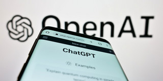 Ein Smartphone, auf dem die Webseite "ChatGPT" geöffnet ist, vor einem Logo von OpenAI.