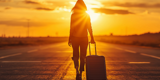 Eine junge Frau mit Rollkoffer geht in den Sonnenuntergang