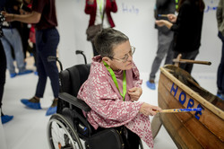Eine Frau im Rollstuhl schreibt mit blauer Farbe auf ein Holzboot