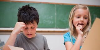 Ein Junge und ein Mädchen sitzen vor einer Tafel und bearbeiten Arbeitsblätter