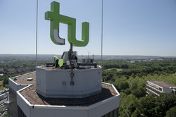 TU Logo Reparatur 1 Menschen nehmen ein Teil der grünen Verkleidung des Logos ab, um es von innen zu reinigen.
