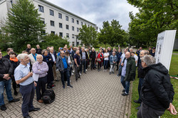 rechts im Bild stehen die vier Ehrengäste, links stehen viele weitere Gäste, die zuhören