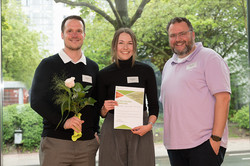 In the photo, three people are smiling at the camera after the certificates were presented.