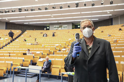 Ein Mann mit Mundschutz und Schutzhandschuhen hält ein Mikrofon in der Hand, das durch eine Folie geschützt ist