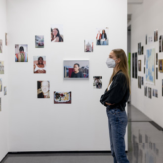 Frau steht seitlich in einem Ausstellungsraum und betrachtet die Ausstellungsobjekte