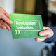Eine Postkarte mit der Aufschrift "Konklusion? Inklusion!" wird von einer Hand zur anderen gereicht.