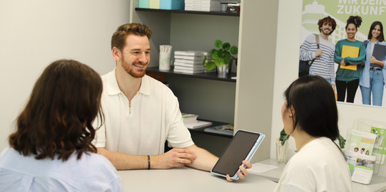 Beratungssituation ZSB 3 Studienberater berät zwei Studierende am Beratungstisch. Er hält ein Tablet zur Beratung in der Hand.