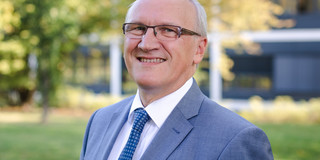 Ein Porträt von einem Mann im Anzug vor einem grünen Baum, der Mann ist Prof. Dirk Biermann.
