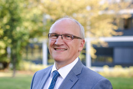 Mai Ein Porträt von einem Mann im Anzug vor einem grünen Baum, der Mann ist Prof. Dirk Biermann.