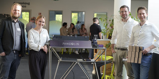 Photo: Four people stand next to a table with a displayed model at an event.