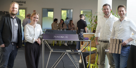 Foto: Vier Personen stehen neben einem Tisch mit einem ausgestellten Modell bei einer Veranstaltung.
