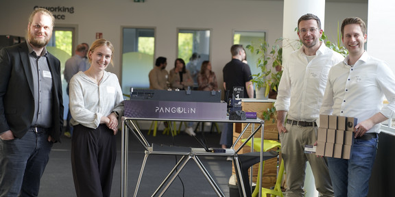 Photo: Four people stand next to a table with a displayed model at an event.