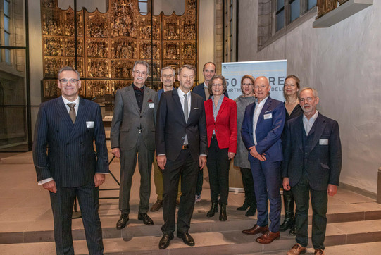 Zehn Personen, darunter drei Frauen und sieben Männer in festlichen Anzügen, blicken in die Kamera. Im Hintergrund ist ein Banner zu erkennen sowie der Altar der der Stadtkirche St. Petri Kirche in Dortmund.