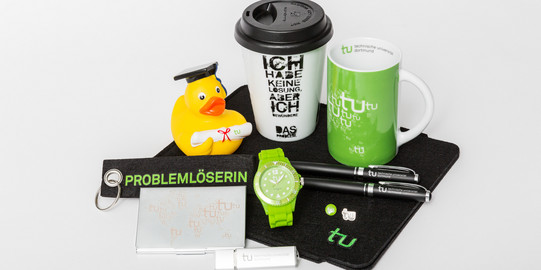 Various TU Dortmund merchandise, including a mug, a watch and a keychain, lie on a table