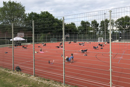 Menschen machen Sportübungen auf einem Sportplatz und halten Abstand ein.