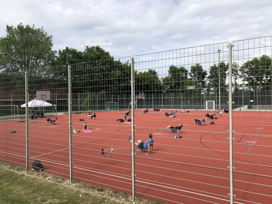 Menschen machen Sportübungen auf einem Sportplatz und halten Abstand ein.