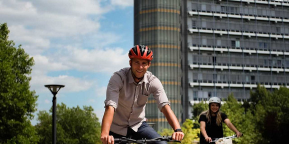 Ein Mann mit einem roten Helm sitzt auf einem Fahrrad und hält an, neben ihm fährt eine Frau mit weißem Helm auf einem Fahrrad.