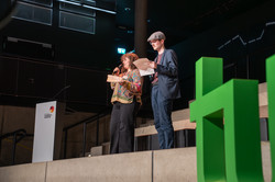 Foto: Zwei Personen moderieren gemeinsam auf einer Bühne.