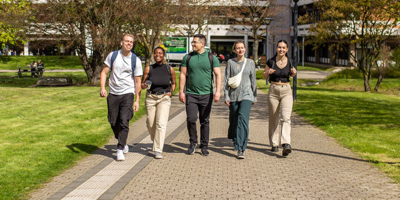Graduates Five people walk in a row across the summer campus, with the building at Emil-Figge-Straße 50 in the background