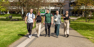 Graduates Five people walk in a row across the summer campus, with the building at Emil-Figge-Straße 50 in the background