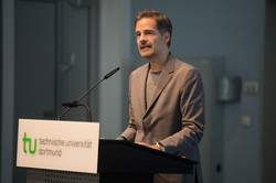 Prof. Christoph Schuck, ein Mann mit kurzen, dunklen Haaren und sehr kurzem Bart, steht an einem TU-Rednerpult und spricht.