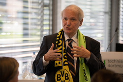 Shaker A. Zahra spricht vor einem Publikum. Er trägt einen BVB- und TU Dortmund-Schal