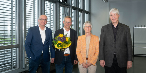 Vier Personen stehen in einer Reihe und lächeln in die Kamera. V.l.n.r: Prof. Manfred Bayer, Markus Neuhaus mit einem Blumenstrauß, Prof. Johanna Weber und Prof. Lorenz Schwachhöfer.