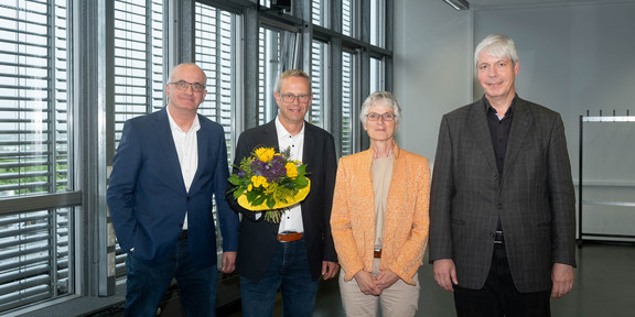 Four people stand in a row and smile at the camera. From left to right: Prof. Manfred Bayer, Markus Neuhaus with a bouquet of flowers, Prof. Johanna Weber and Prof. Lorenz Schwachhöfer.