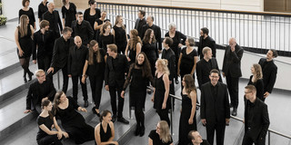 Der Kammerchor der TU Dortmund Ein Gruppenfoto vom Kammerchor der TU Dortmund. Die schwarz gekleideten Musiker*innen sind von halboben fotografiert.