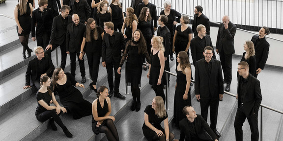 Der Kammerchor der TU Dortmund Ein Gruppenfoto vom Kammerchor der TU Dortmund. Die schwarz gekleideten Musiker*innen sind von halboben fotografiert.