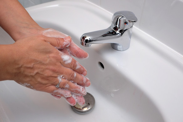 Eingeseifte Hände über einem Waschbecken, aus dem Hahn kommt kaltes Wasser