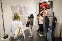 Foto: Mehrere Personen befinden sich in der Kunstausstellung, schauen sich die Werke an und machen Fotos.