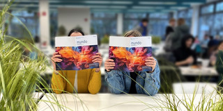 Foto: Zwei Personen sitzen an einem Tisch und zeigen die Zeitschrift „mundo“.