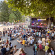 Viele Menschen sitzen auf Bierbänken vor einer Bühne auf der Live-Musik gespielt wird. 