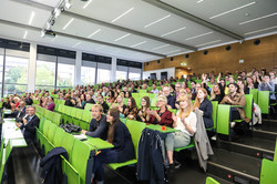 Ein vollbesetzter Hörsaal mit grüner Bestuhlung.