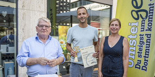 Gruppenfoto: Christoph Edeler, Leiter des Hochschulsports, steht zwischen einem Mann und einer Frau und hält eine Urkunde und einen Pokal in der Hand.