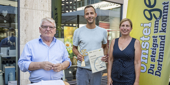 Gruppenfoto: Christoph Edeler, Leiter des Hochschulsports, steht zwischen einem Mann und einer Frau und hält eine Urkunde und einen Pokal in der Hand.