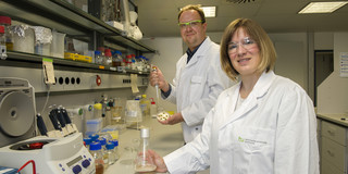 Two people in white coats are standing in a laboratory.