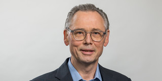 A photo of a man with glasses wearing a blue shirt and jacket.