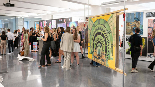Das Bild zeigt einen großen Ausstellungssaal mit zahlreichen Personen und großen bunten Kunstwerken.