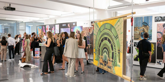Das Bild zeigt einen großen Ausstellungssaal mit zahlreichen Personen und großen bunten Kunstwerken.