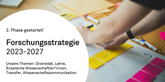 Foto mit Text: Das Foto zeigt Hände, die bunte Post-It-Zettel auf einem Plakat arrangieren. In einem weißen Kreis steht folgender Text: "2. Phase gestartet! Forschungsstrategie 2023-2027, Unsere Themen: Diversität, Lehre, Exzellente Wissenschaftler*innen, Transfer, Wissenschaftskommunikation"